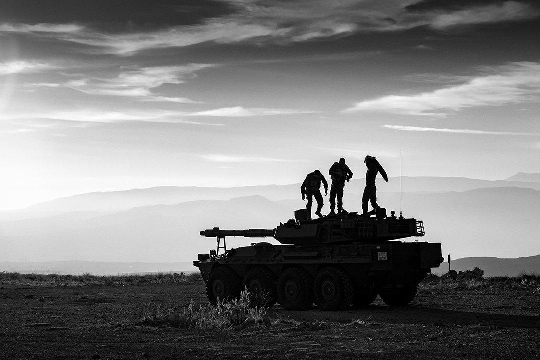 Silhouettes of service members on a vehicle in front of mountains.